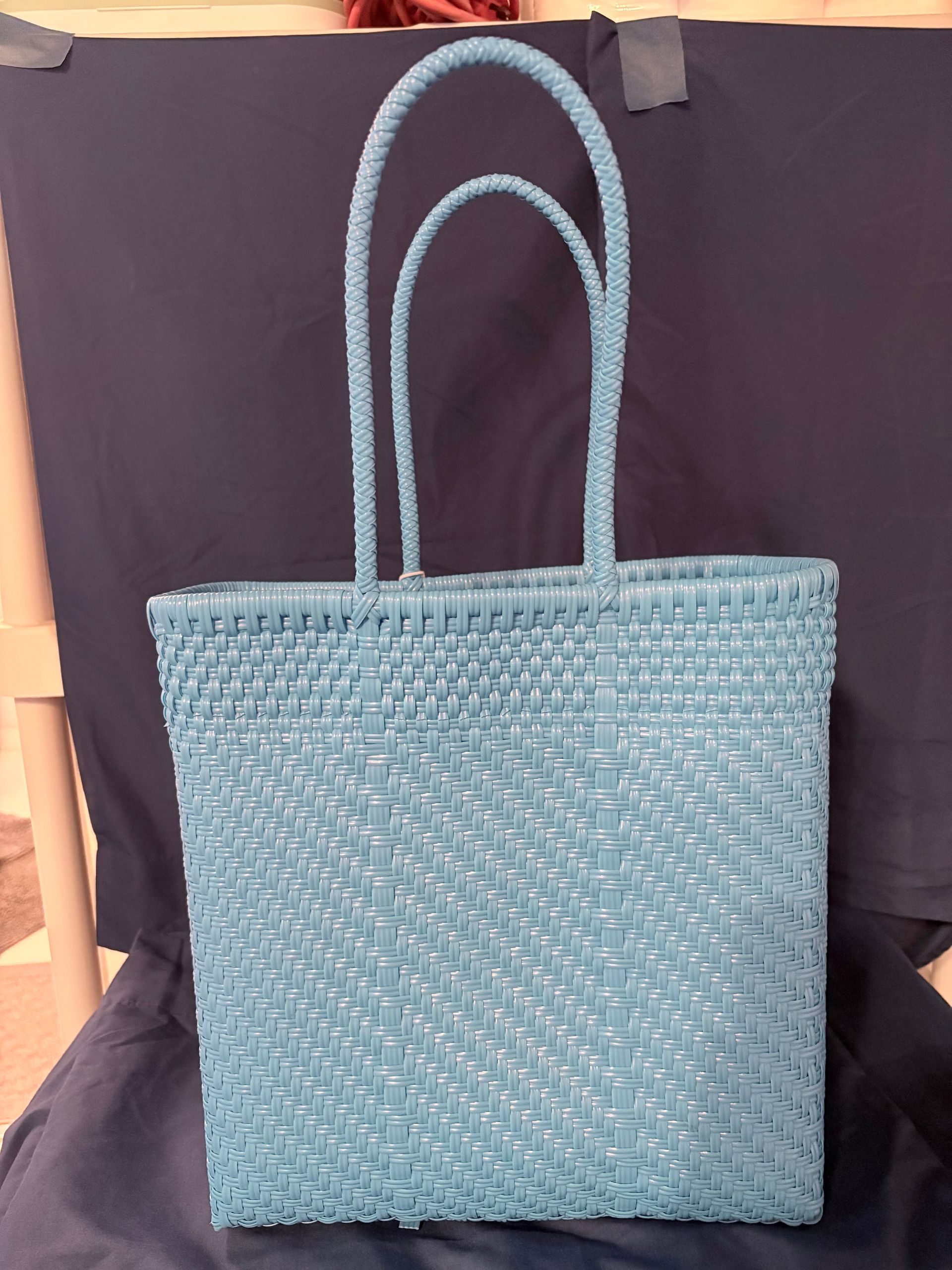 Blue woven tote bag with double handles against a dark backdrop