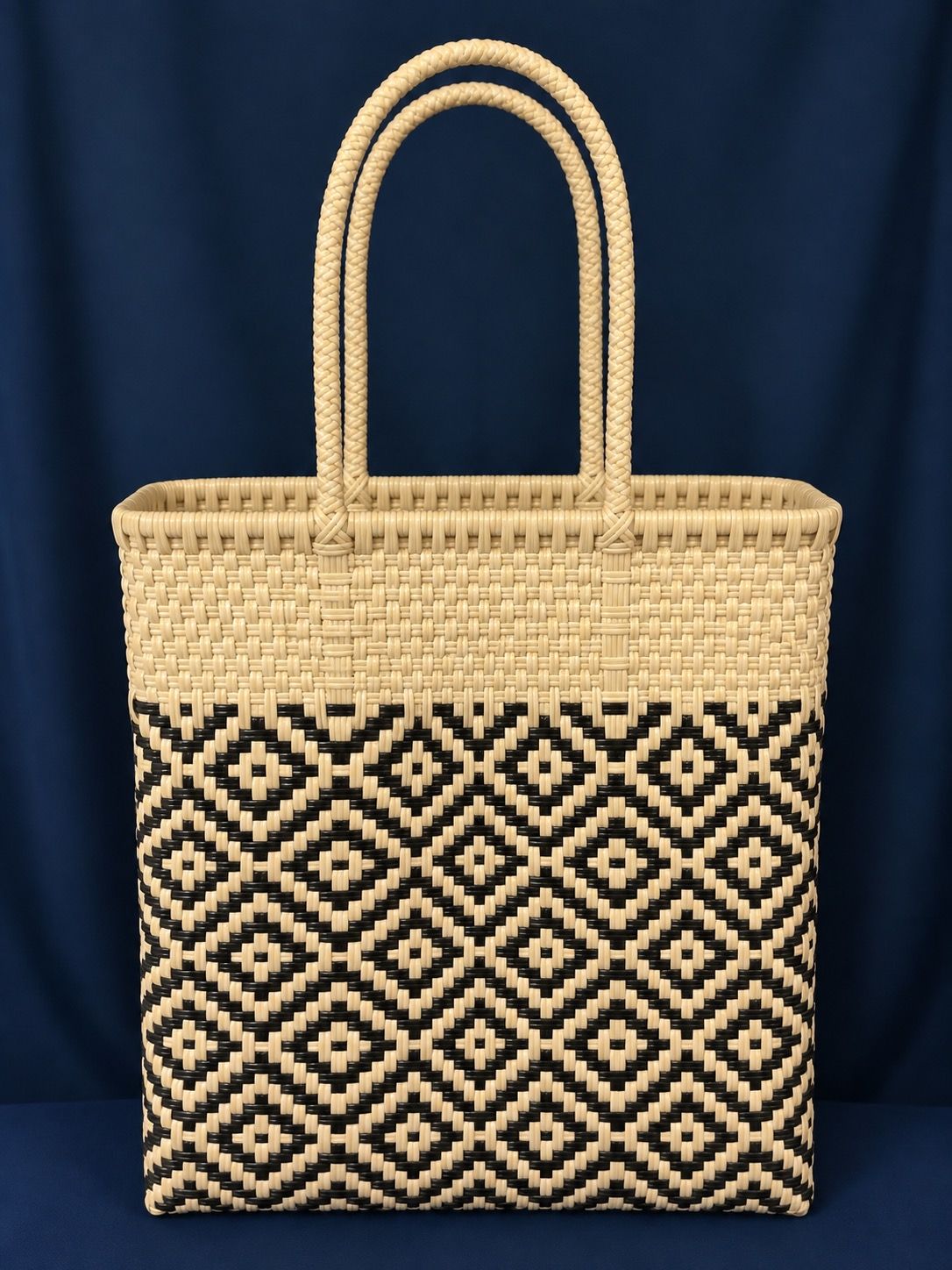 Woven straw tote bag with black-and-cream geometric pattern and double loop handles on a dark background