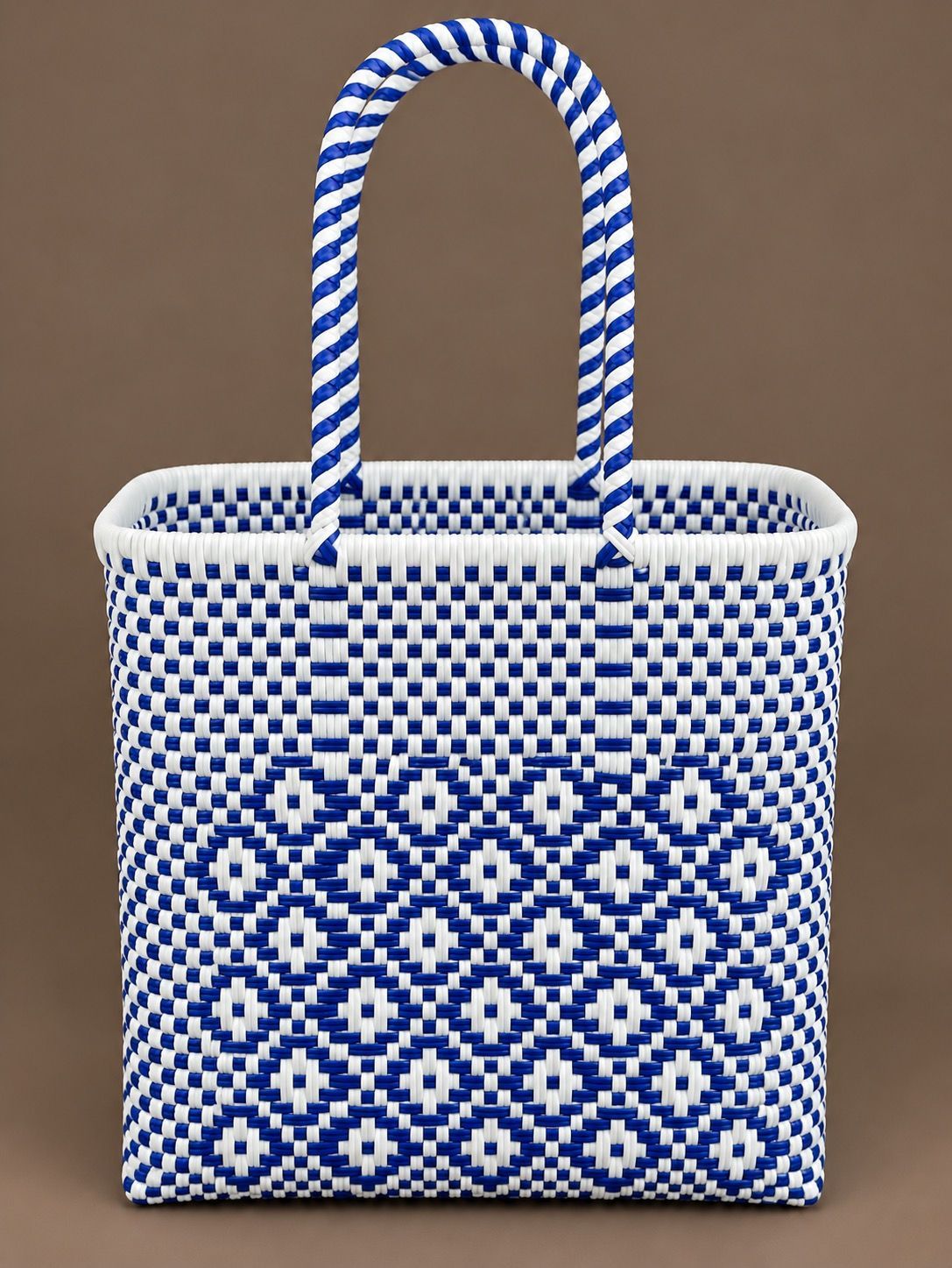 Blue patterned woven tote on a picnic table, filled with flowers, bread, sunglasses, and a lemon.