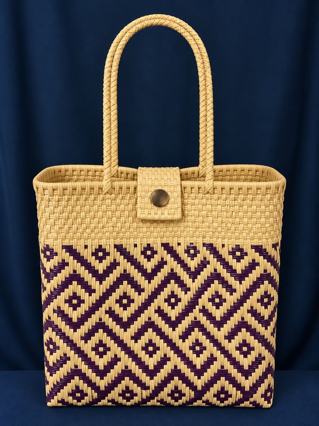 Woven straw tote bag with purple geometric pattern and tall handles against a dark blue background