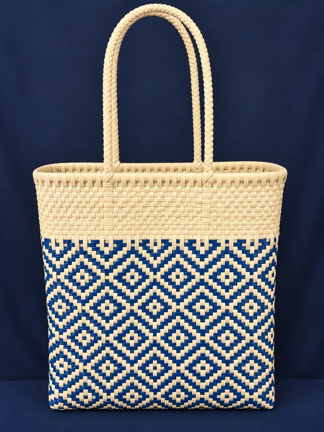 Woven straw tote bag with tan handles and navy geometric pattern