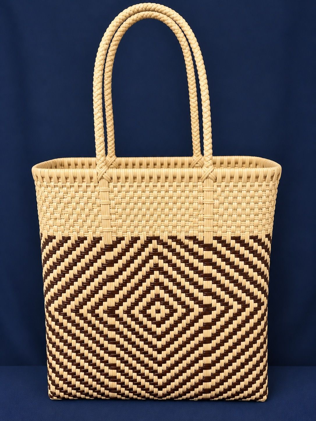 Woven straw tote bag with tan handles and black-and-tan geometric pattern on a dark blue background