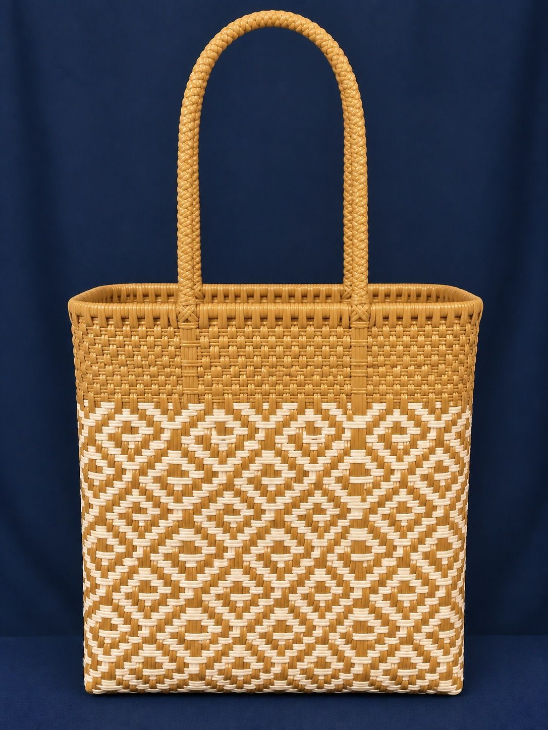 Woven straw tote bag with tan handles and a white geometric pattern on a dark background