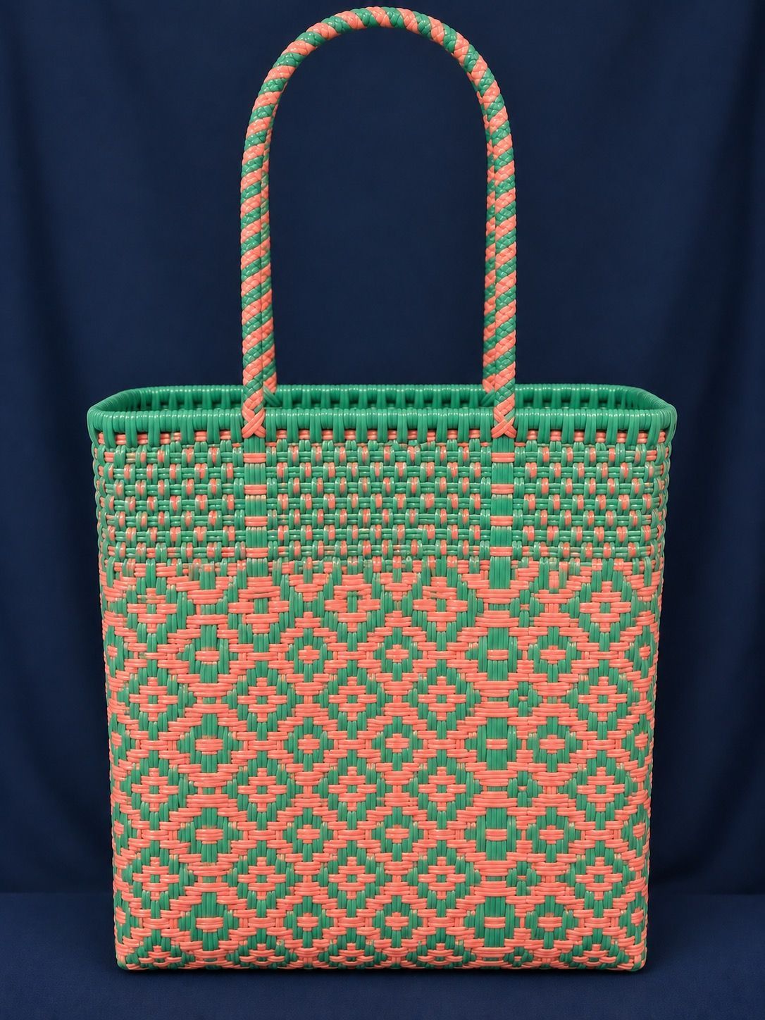 Green-and-orange woven tote bag with long braided handles on a dark background