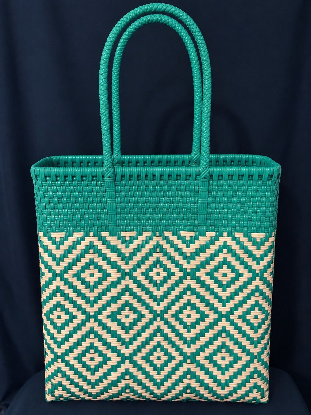 Green woven tote bag with tan geometric pattern and twin handles against a dark background