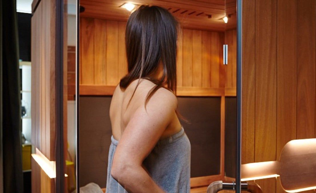 A woman wrapped in a towel is standing in a sauna.