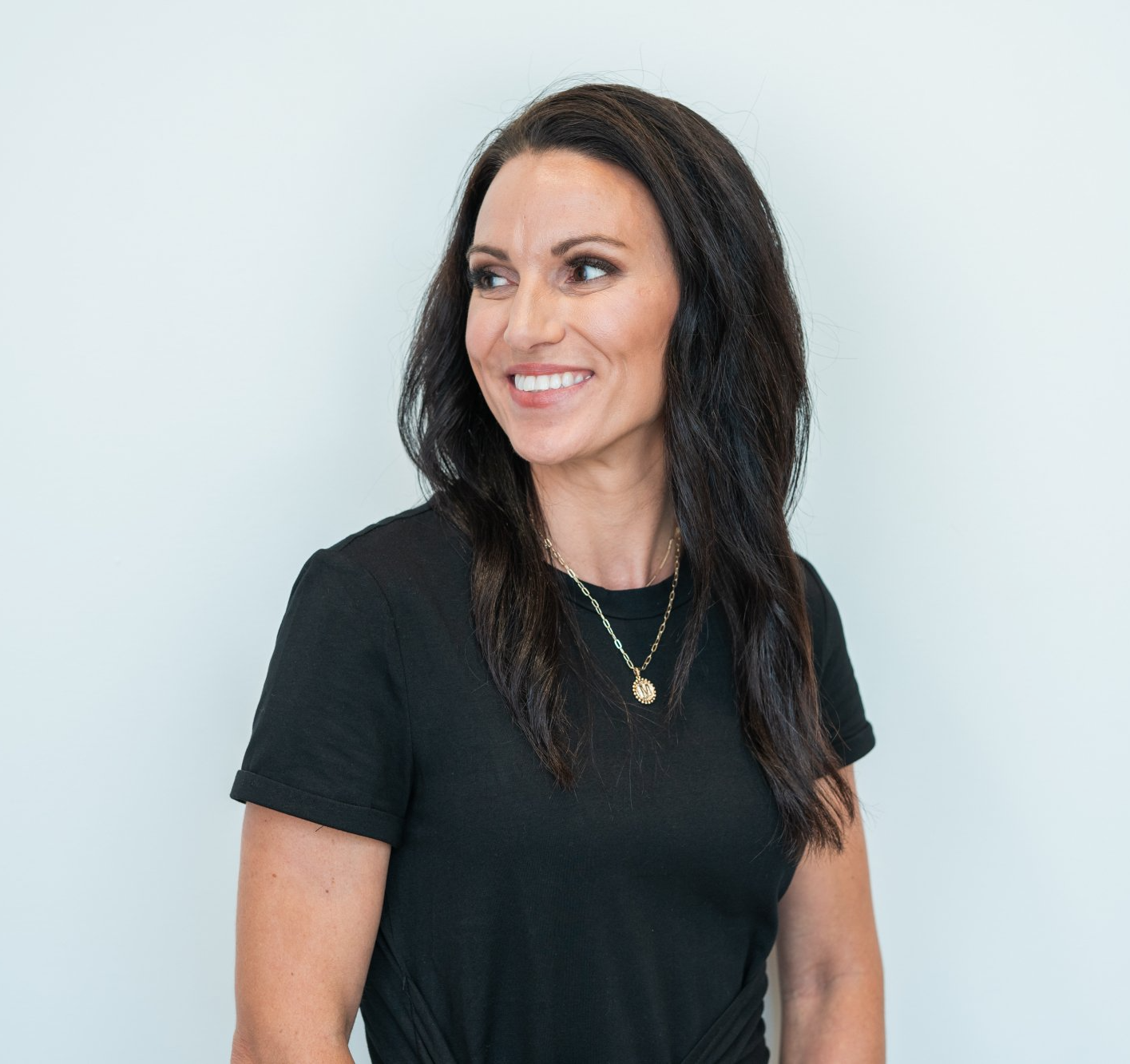 A woman wearing a black shirt and a necklace is smiling.