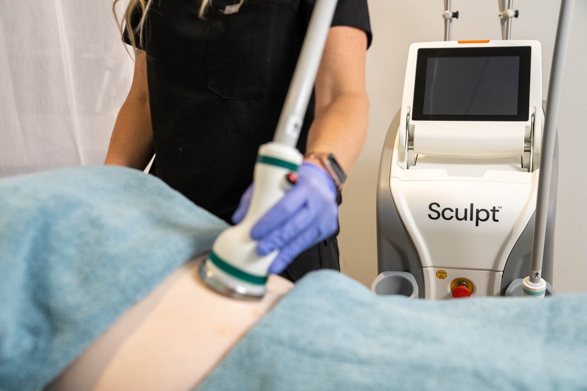 A woman is using a sculpt machine on a patient 's stomach.