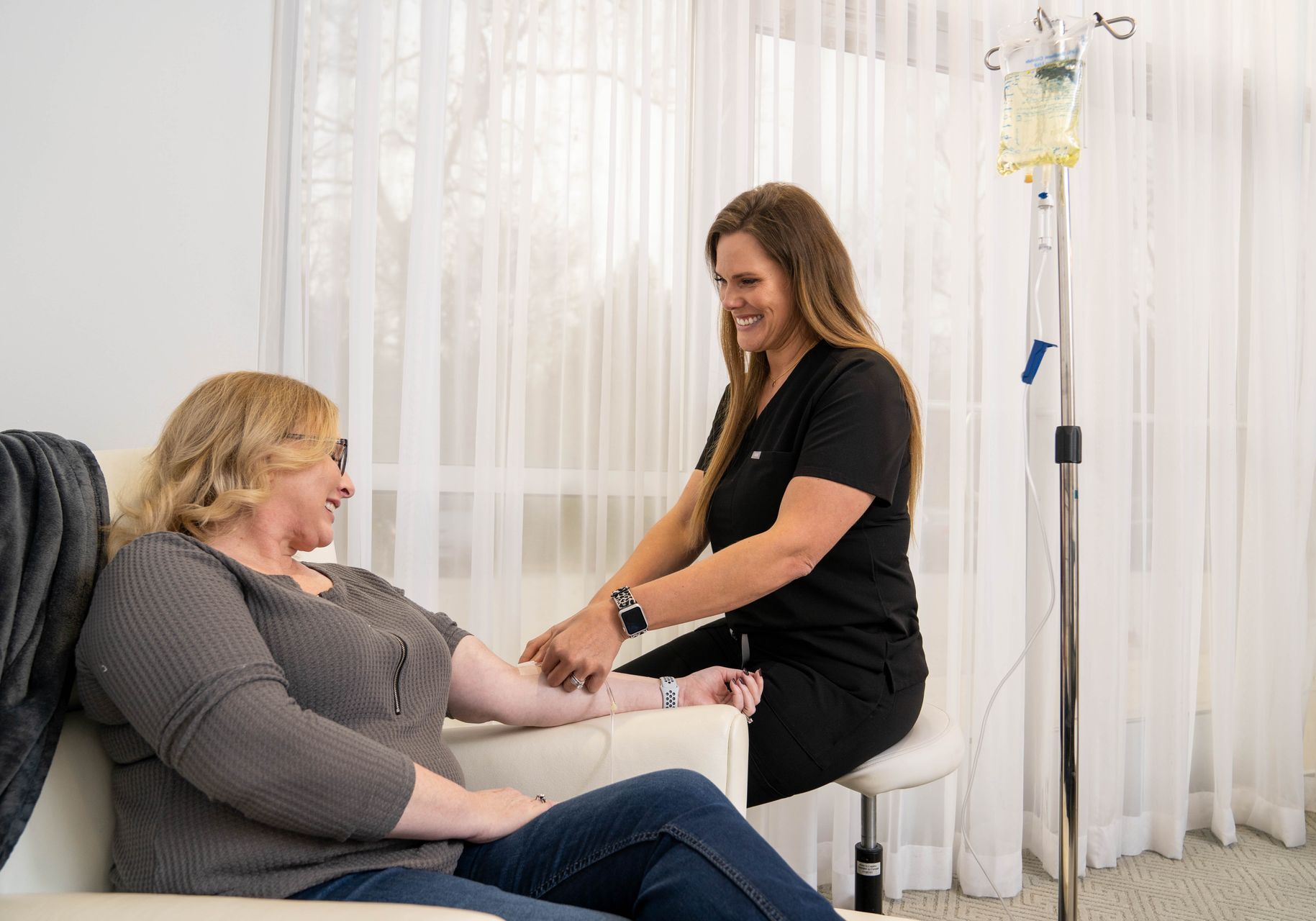 A woman is sitting on a couch getting an injection from a nurse.
