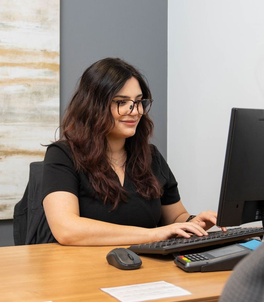 A woman is sitting at a desk typing on a computer keyboard.