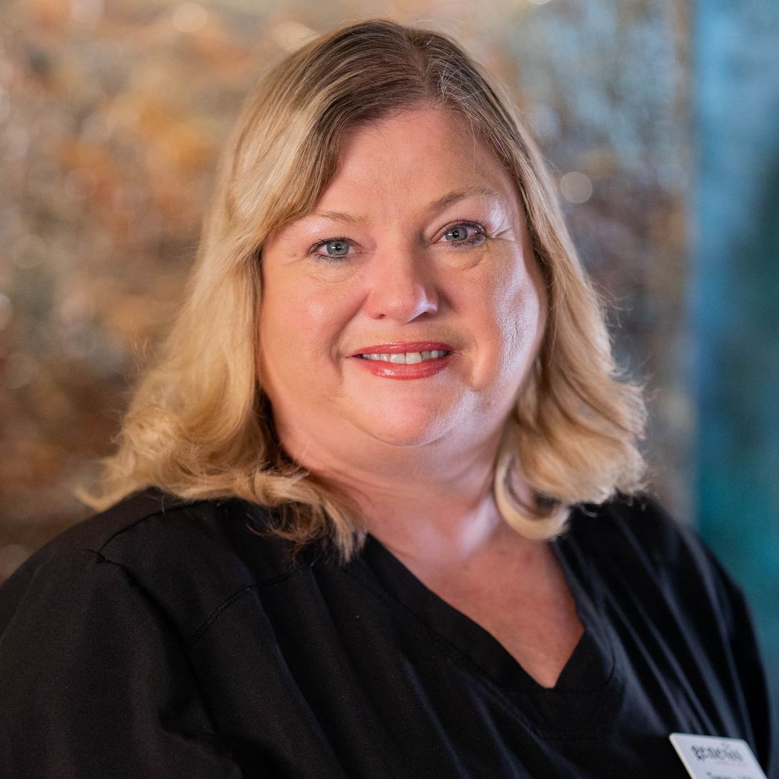 A woman in a black scrub top is smiling for the camera.