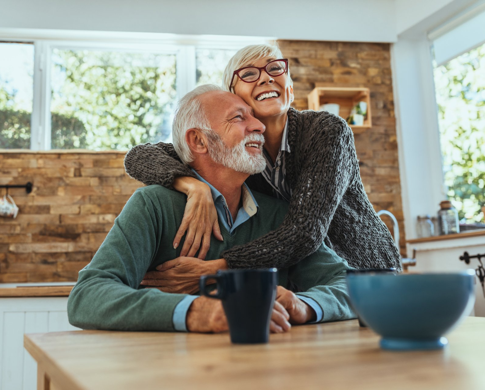 A woman is hugging an older man while sitting at a table.
