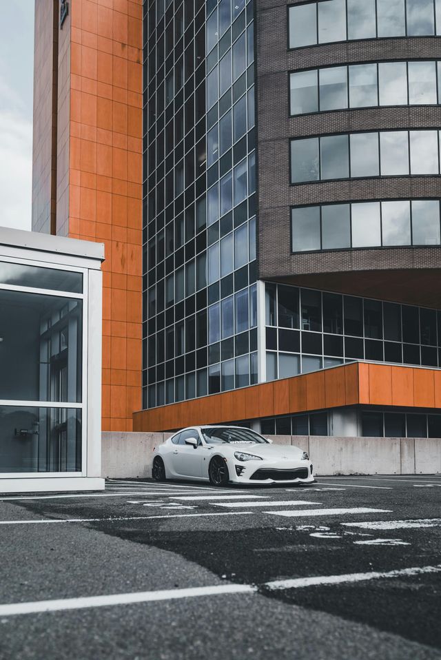 A white car is parked in front of an orange building