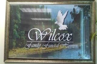 Framed sign for Wilcox Family Funeral Home with white dove logo and script text on a dark background