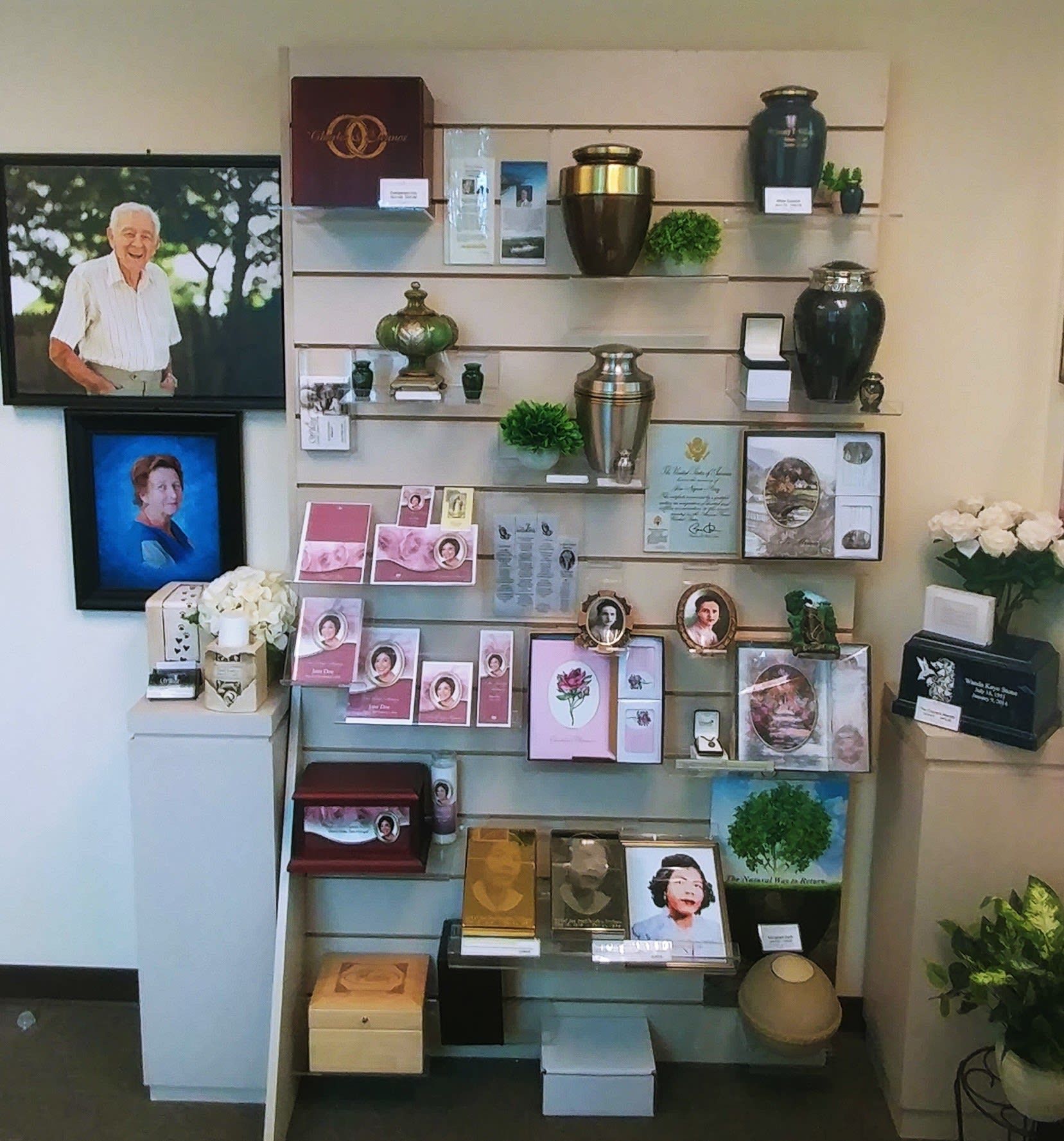 Memorial shelf with framed photos, candles, cards, vases, and flowers on white wall shelving