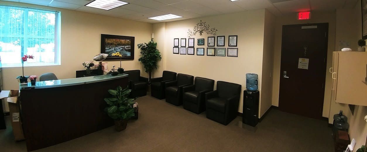 Empty office waiting room with black chairs, front desk, wall art, and an exit door