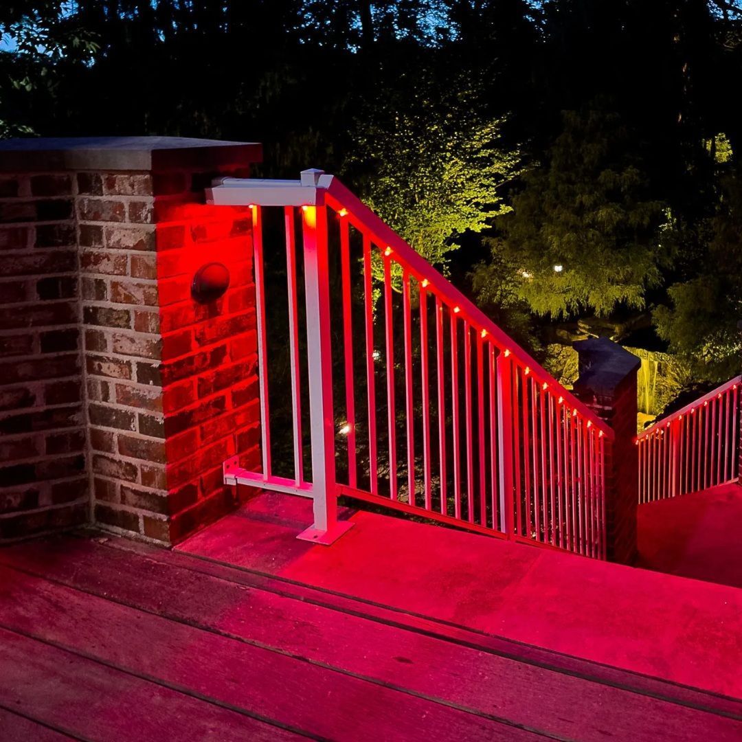 Red-lit wooden deck stairs with white railing beside a brick wall at night