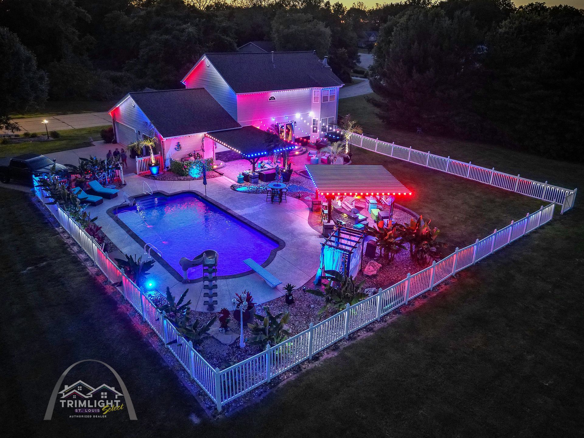 Backyard pool party at night with purple and blue lights, white fence, and a lit house tent.