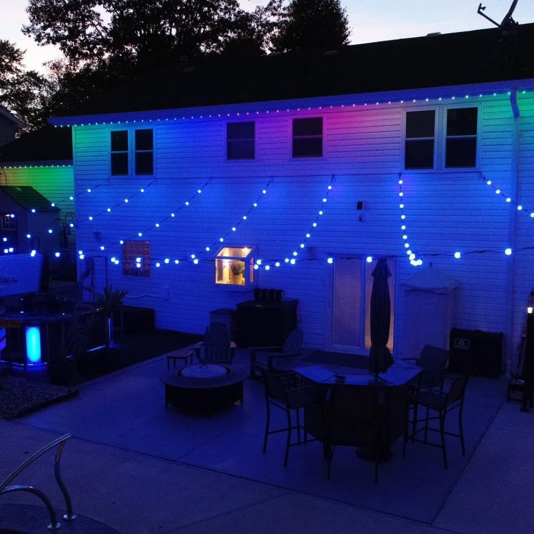 Backyard patio at dusk with blue string lights on a house and outdoor furniture below