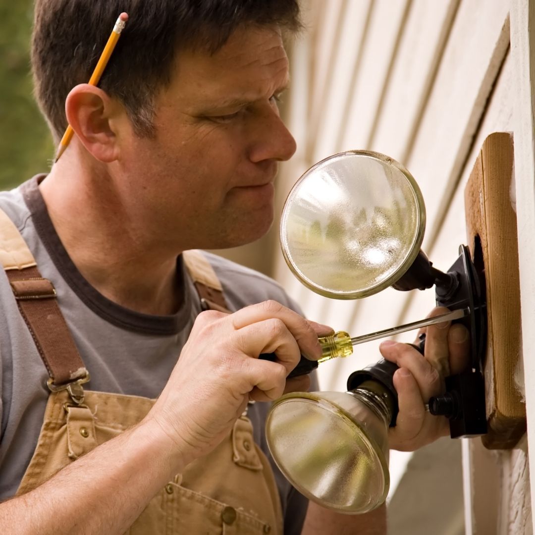 Repairman using a screwdriver to adjust a wall light fixture with suction lamps attached