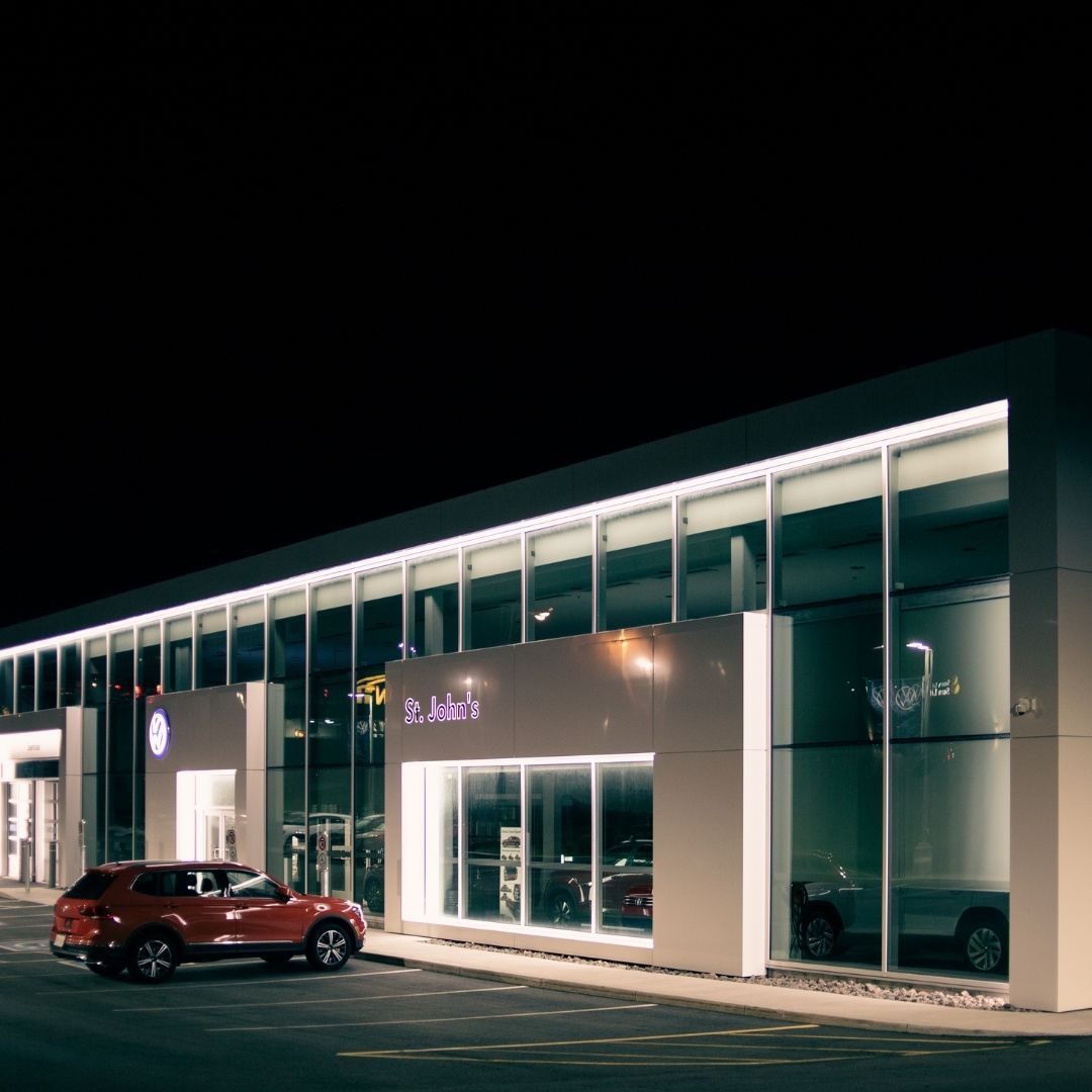 Red SUV parked outside a modern glass-front building at night