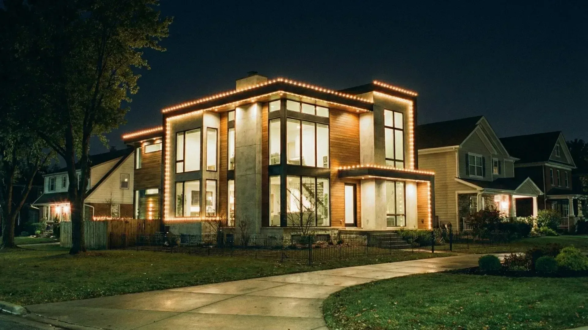Modern two-story house at night with warm interior lights and a driveway in front