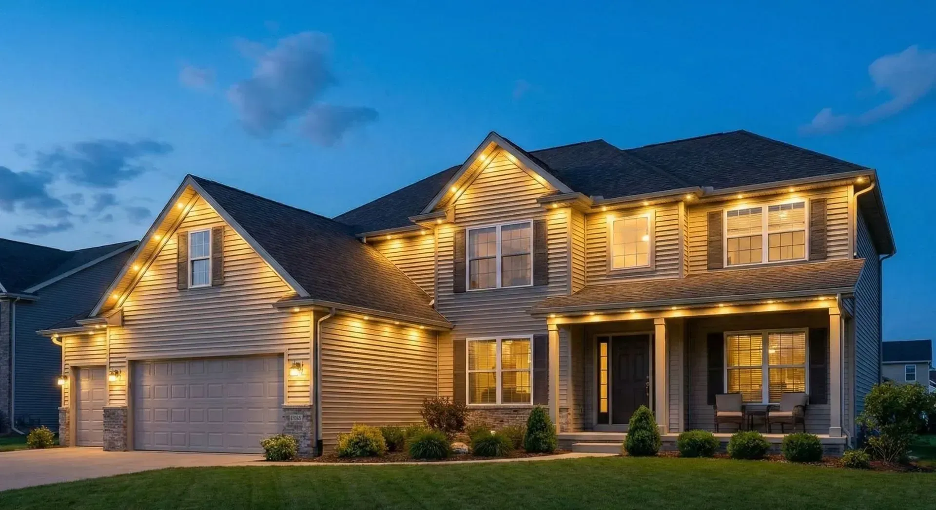 Suburban two-story house at dusk with warm exterior lights and a lit garage
