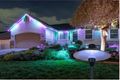 House decorated with colorful Christmas lights at night, with glowing lawn lights and a lit tree in the yard