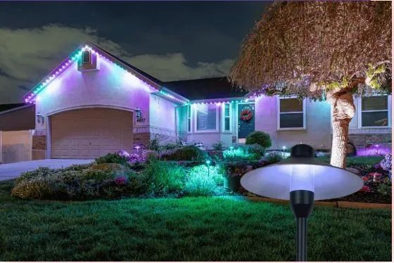 House decorated with colorful Christmas lights at night, with glowing lawn lights and a lit tree in the yard