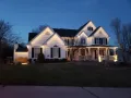 Illuminated white two-story suburban house at dusk with porch lights and a dark lawn