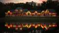A lit house with red and yellow lights reflected in a calm lake at dusk