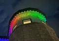 Stone tower lit with rainbow LED lights at night against a dark sky