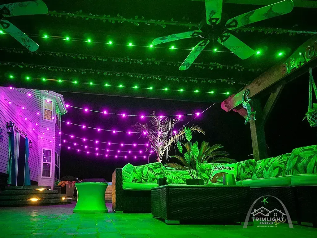 Green and purple-lit outdoor patio with sofas, string lights, and a ceiling fan at night
