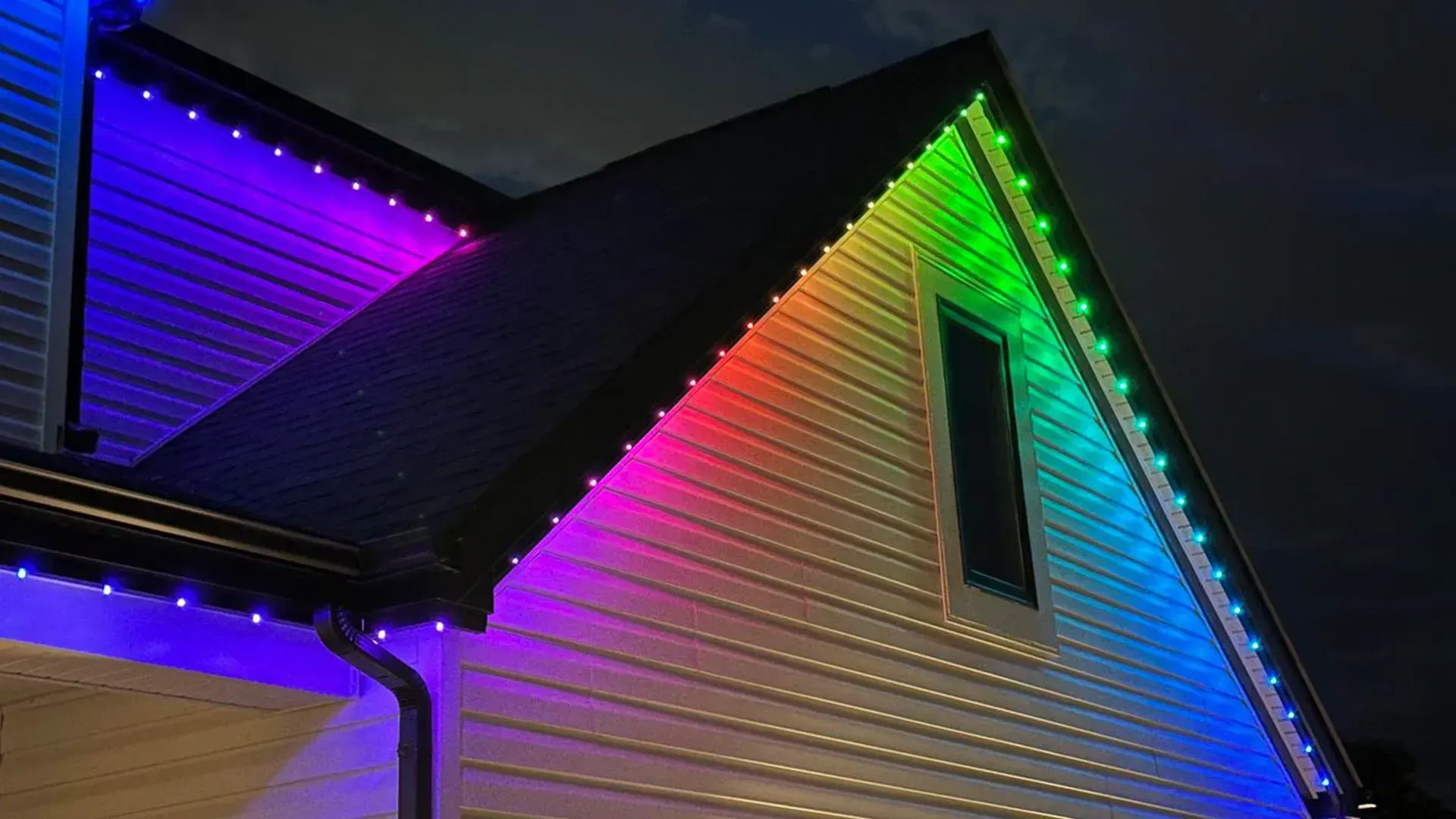 House roofline outlined with colorful rainbow holiday lights at night