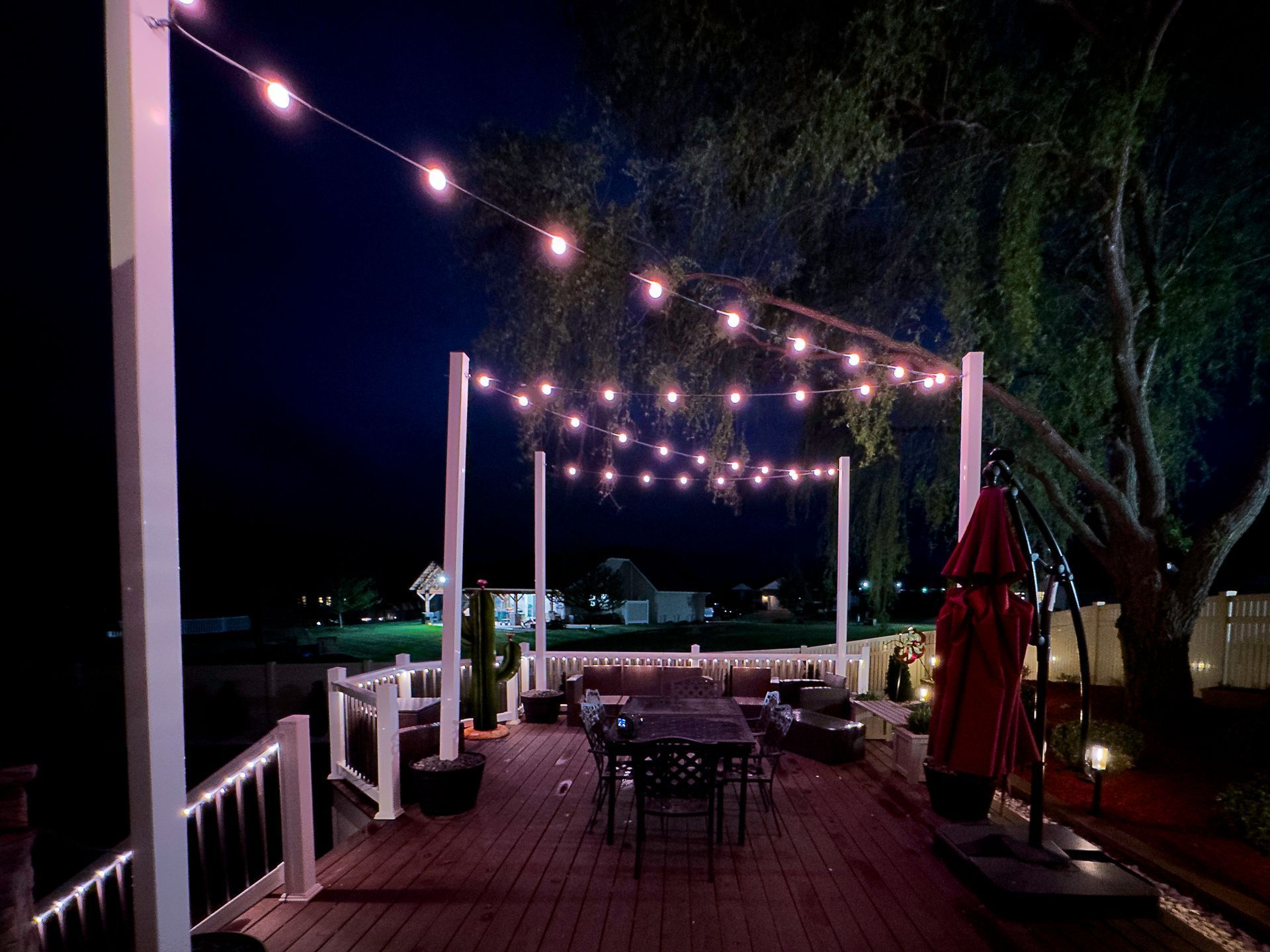 Outdoor patio with string lights, tables, and red umbrellas at night