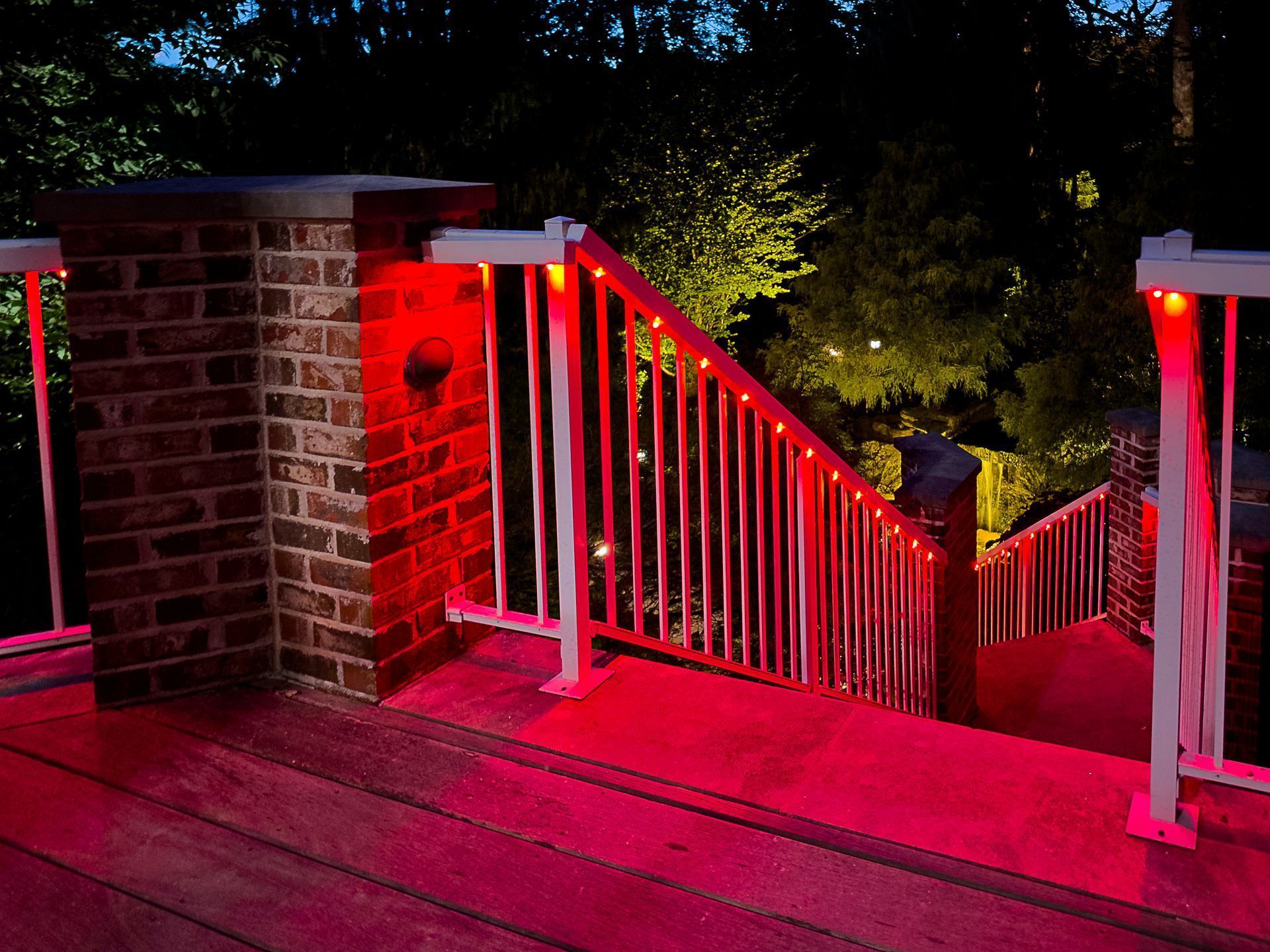 Red-lit wooden staircase and deck descending at night between brick pillars and railings.