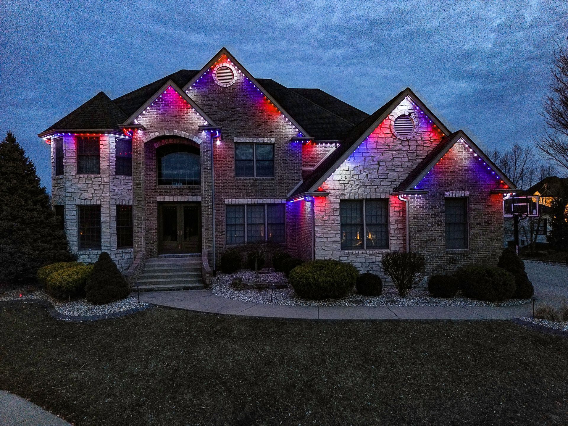 Large suburban house at dusk with purple and red holiday lights on the roof and windows