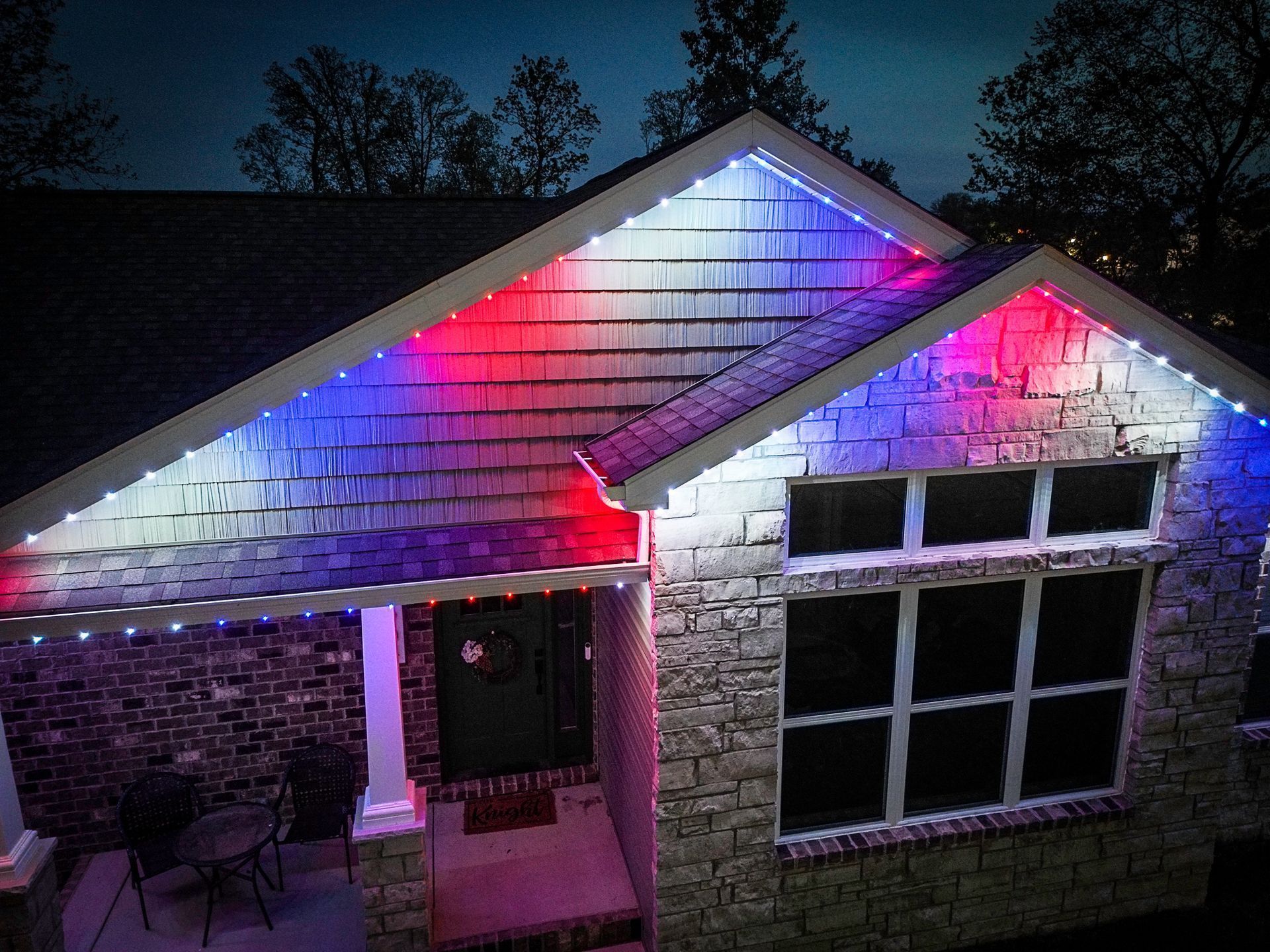 House roof and porch lit with red and blue Christmas lights at night