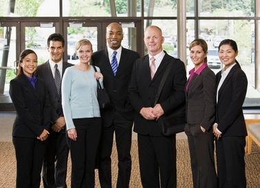 A group of six professionals in business attire standing together in a brightly lit office lobby.
