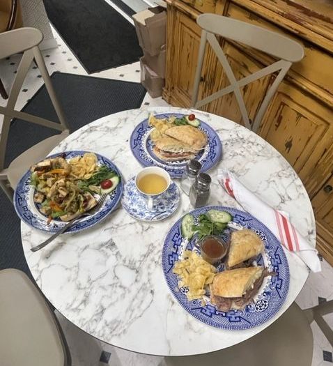 Three blue plates with food on a round white marble table in a cozy café setting