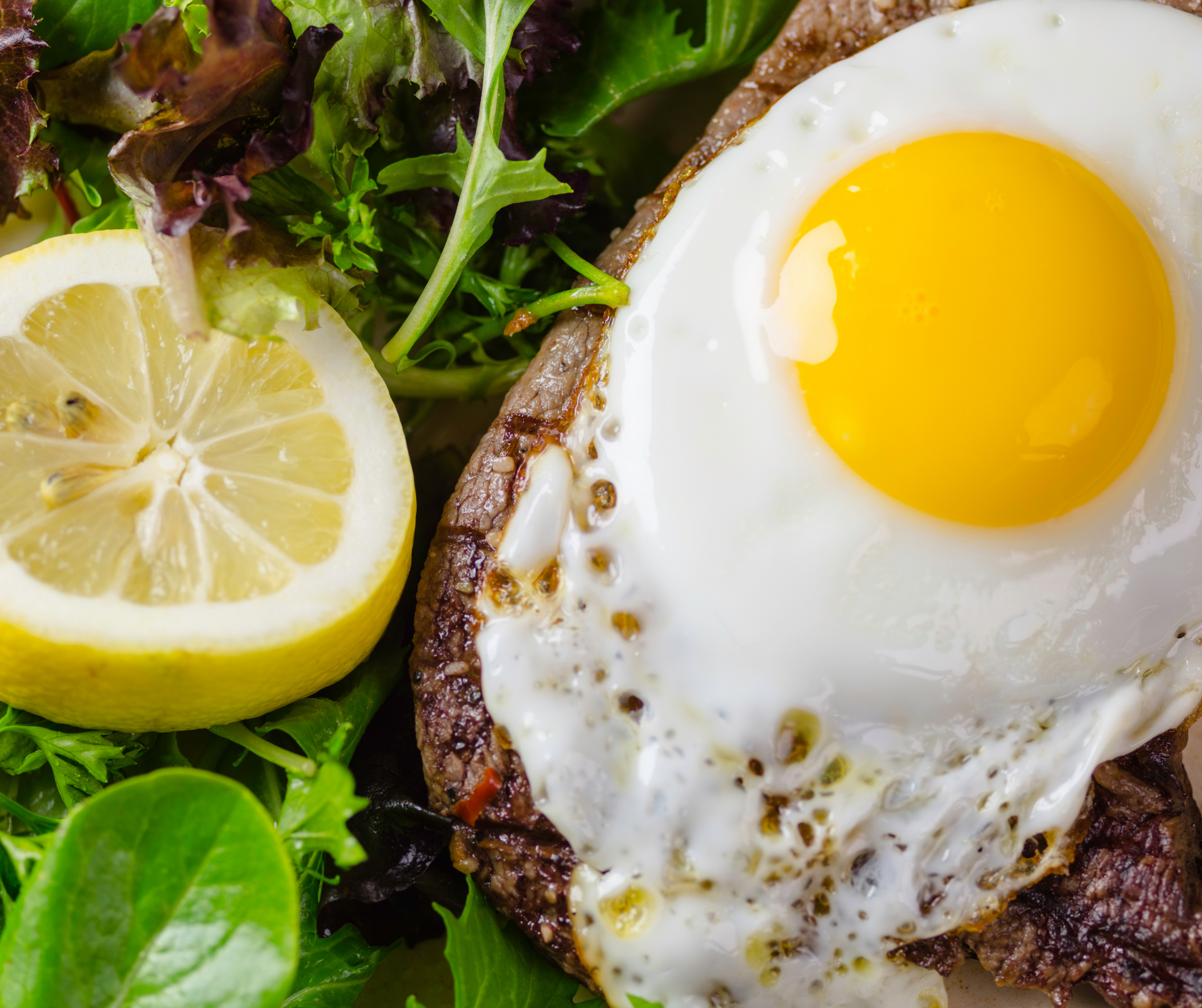 Sunny-side-up egg on a steak with lemon wedge and greens