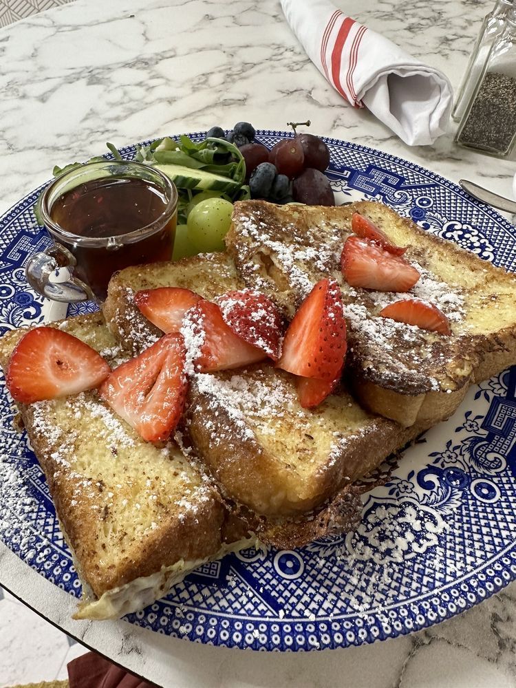 French toast with strawberries, powdered sugar, syrup, and grapes on a blue patterned plate.