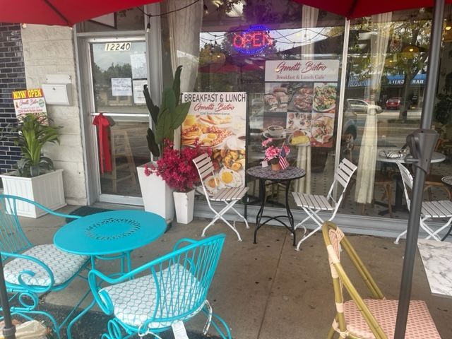 Outdoor café patio with turquoise tables, white chairs, red umbrellas, and storefront windows