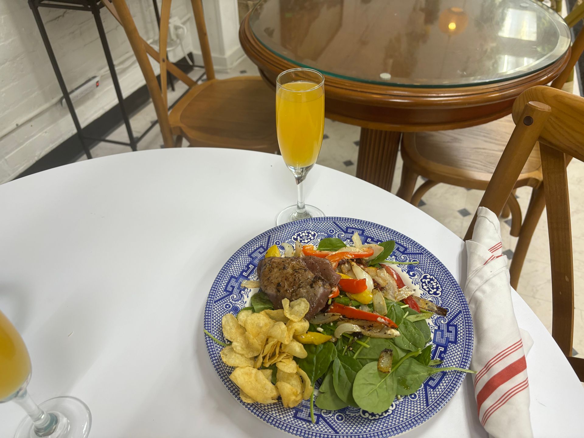 Plate of food on a white table with a glass of orange drink and a round glass-topped chair nearby