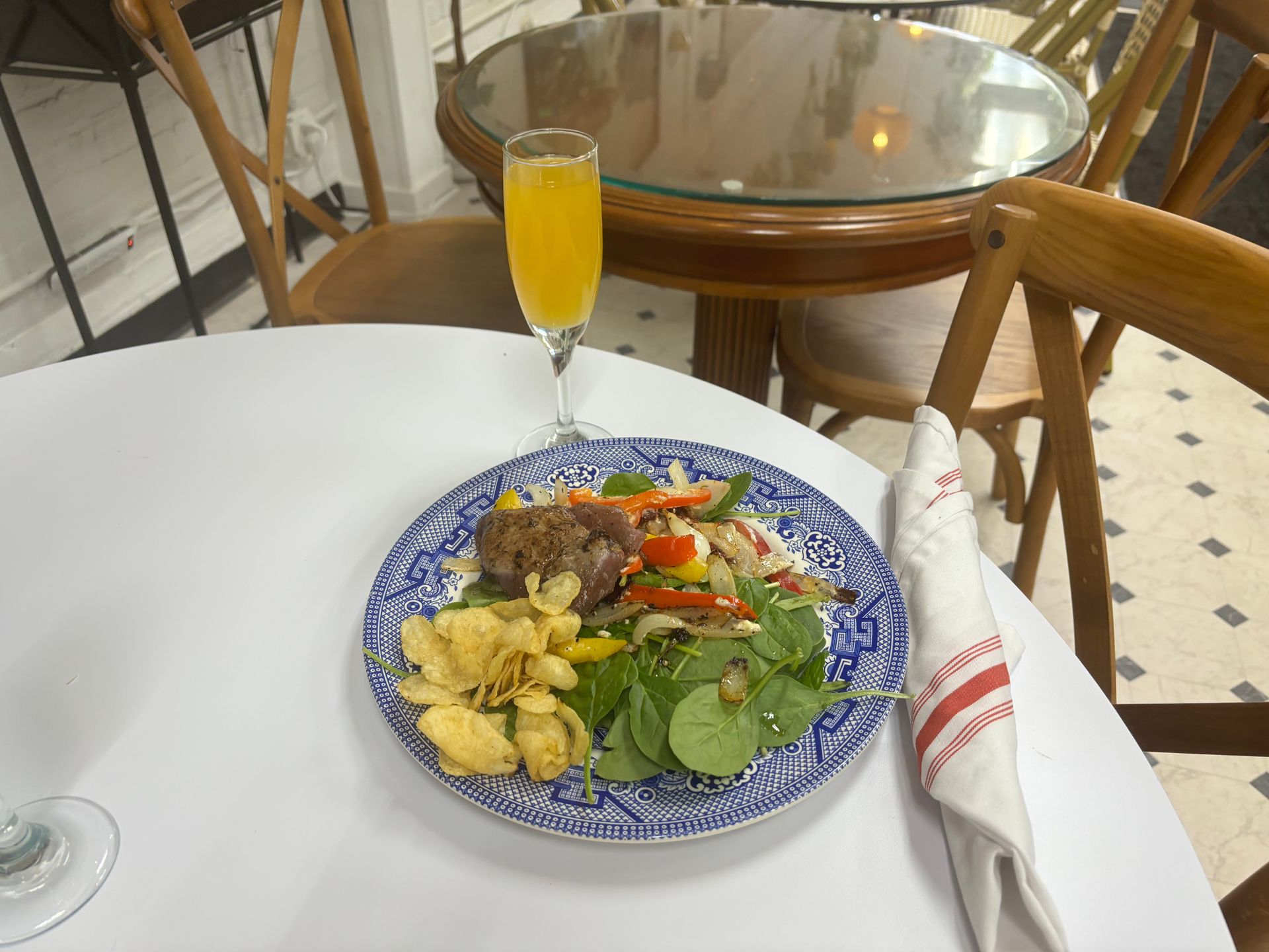 Restaurant table with blue plate of food, yellow drink, and folded napkin on a white tablecloth
