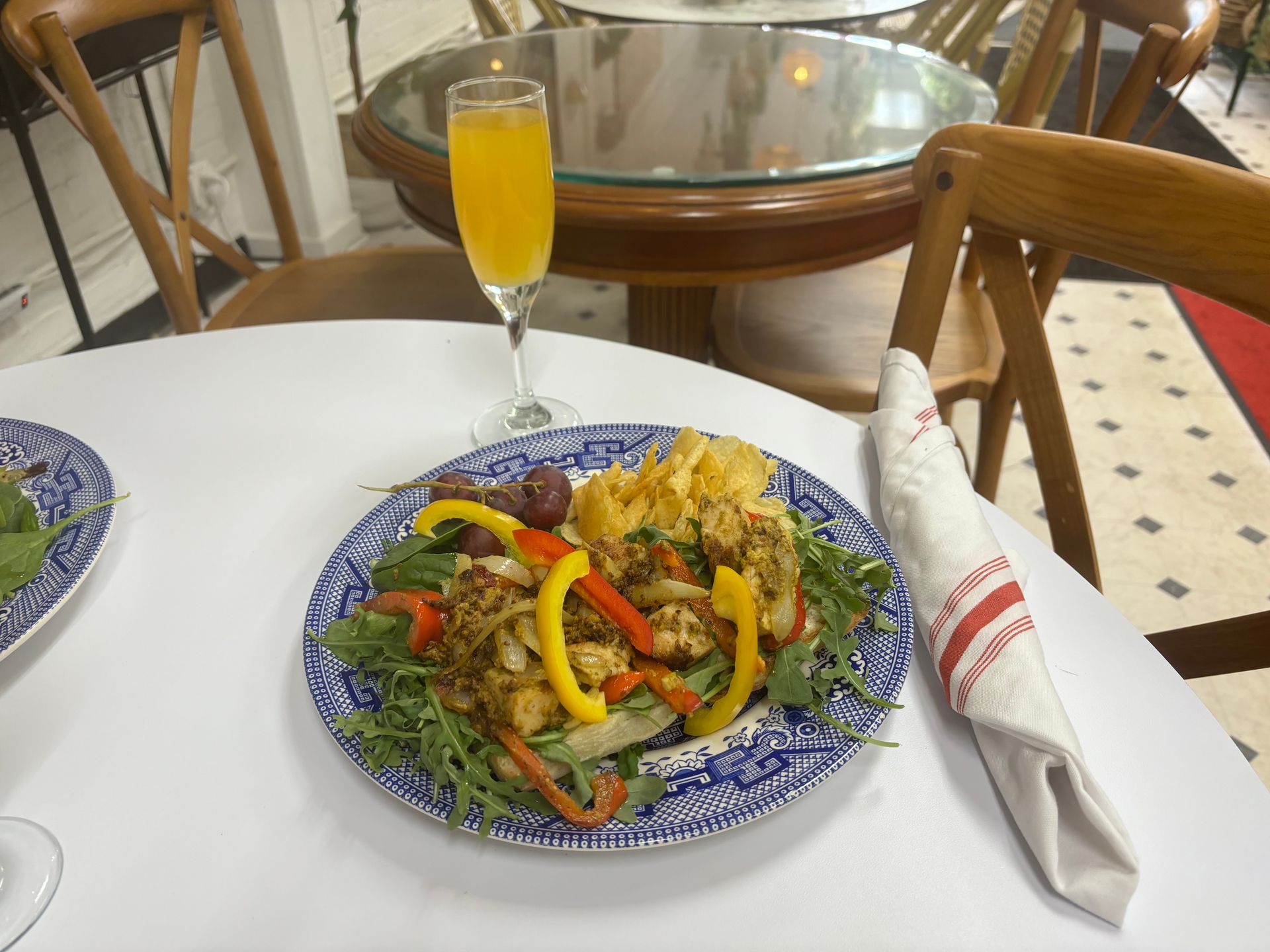 Plated meal with vegetables on a table, with a glass of orange drink and rolled napkin nearby