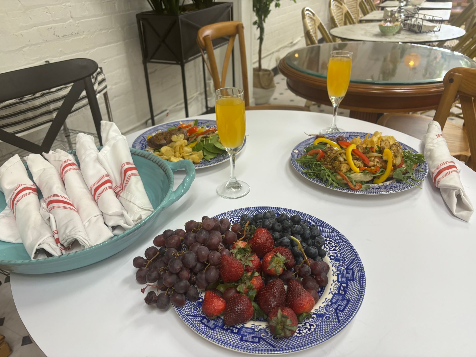 Outdoor table set with fruit, salad plates, orange drinks, and rolled napkins on a patio