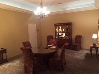 Formal living room with round table, upholstered chairs, chandelier, and cabinet against beige walls.