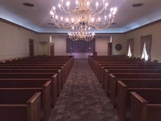 Empty church interior with wooden pews, central aisle, and a large chandelier ceiling light