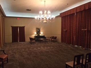 Elegant banquet hall with chandelier, long drapes, and a piano near the back wall.